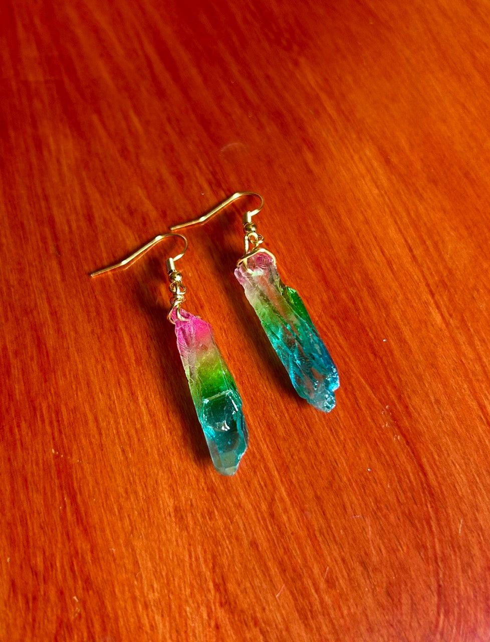 Rainbow crystal earrings with gold color fishhook earwire on a wooden surface.