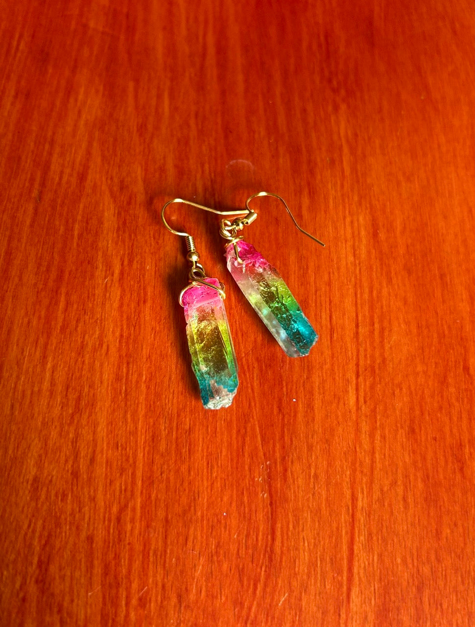 Rainbow crystal earrings with gold color fishhook earwire on a wooden surface.