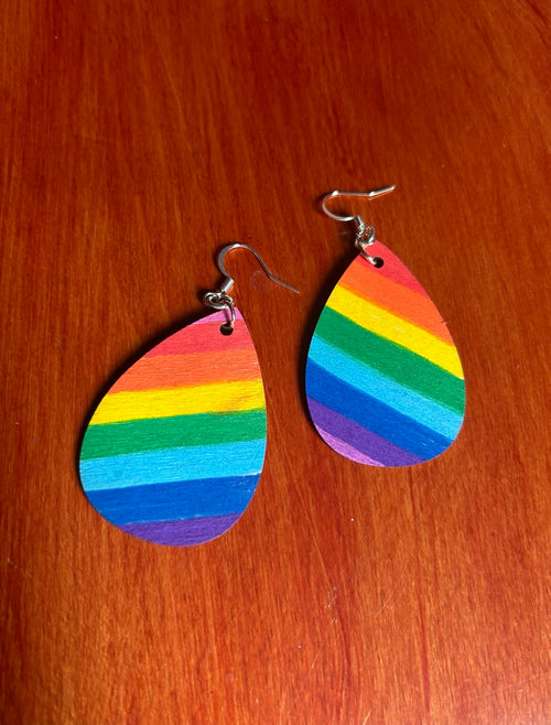 Back side of teardrop-shaped wooden earrings with angles horizontal rainbow stripes. Includes silver fishhook wires on a red-brown wooden surface.