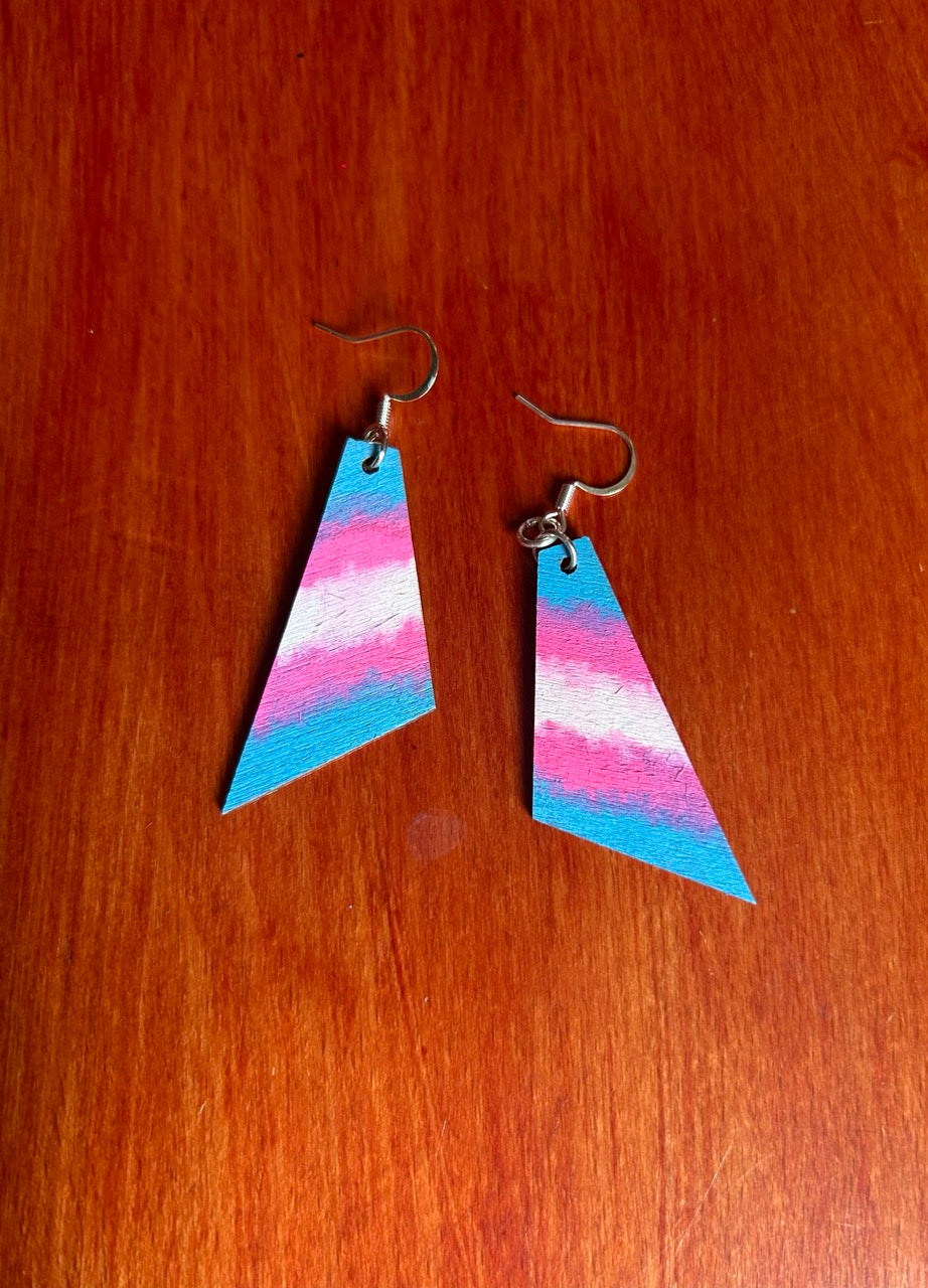 Backside of handmade geometric dangle earrings with a pink, white, and blue horizontal striped pattern, hanging from silver fishhook wires on a wooden surface.