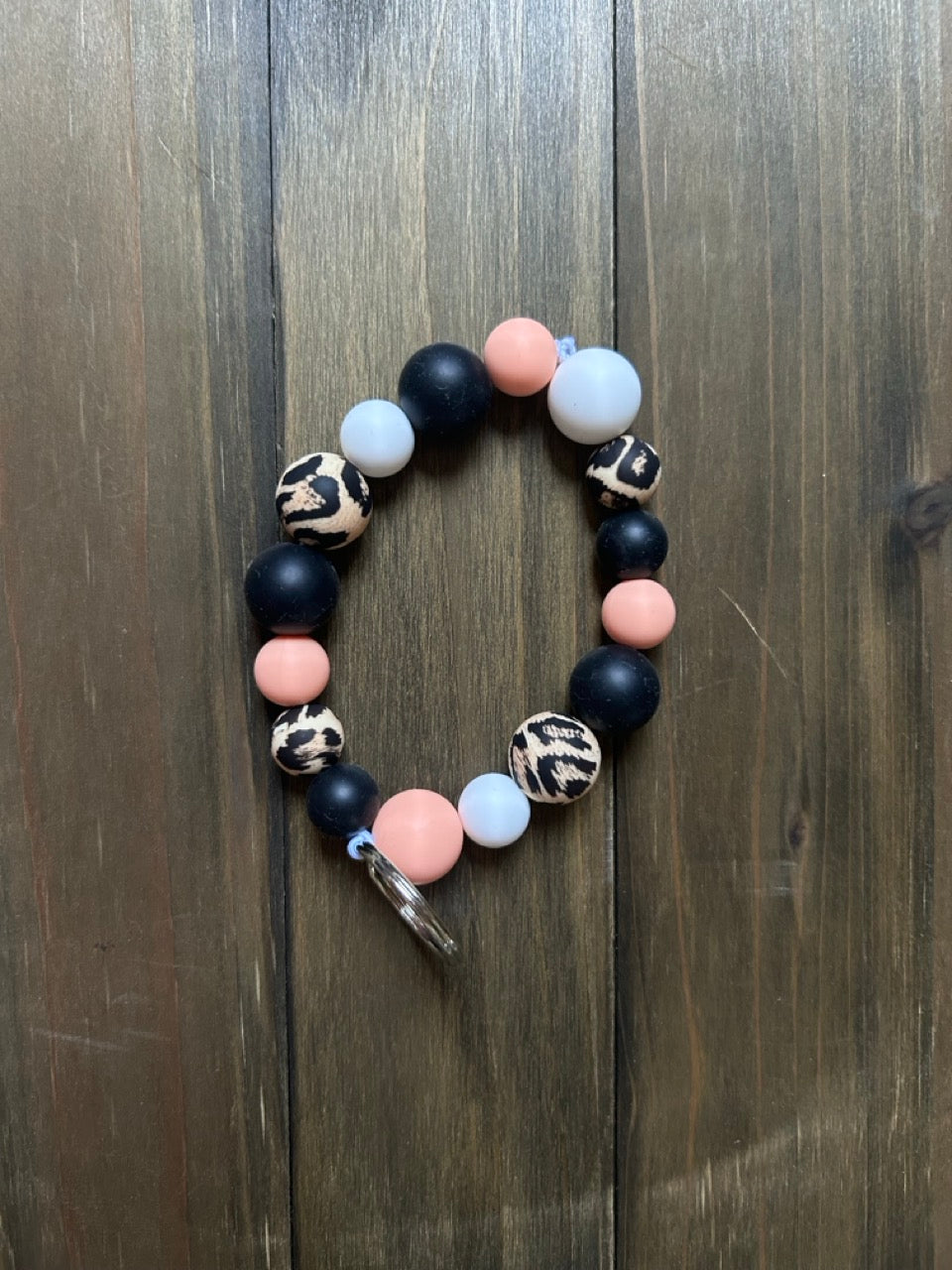 Silicone beaded wristlet with black, peach, white, and leopard print beads. A silver key ring is attached, and it is displayed on a dark wood background.