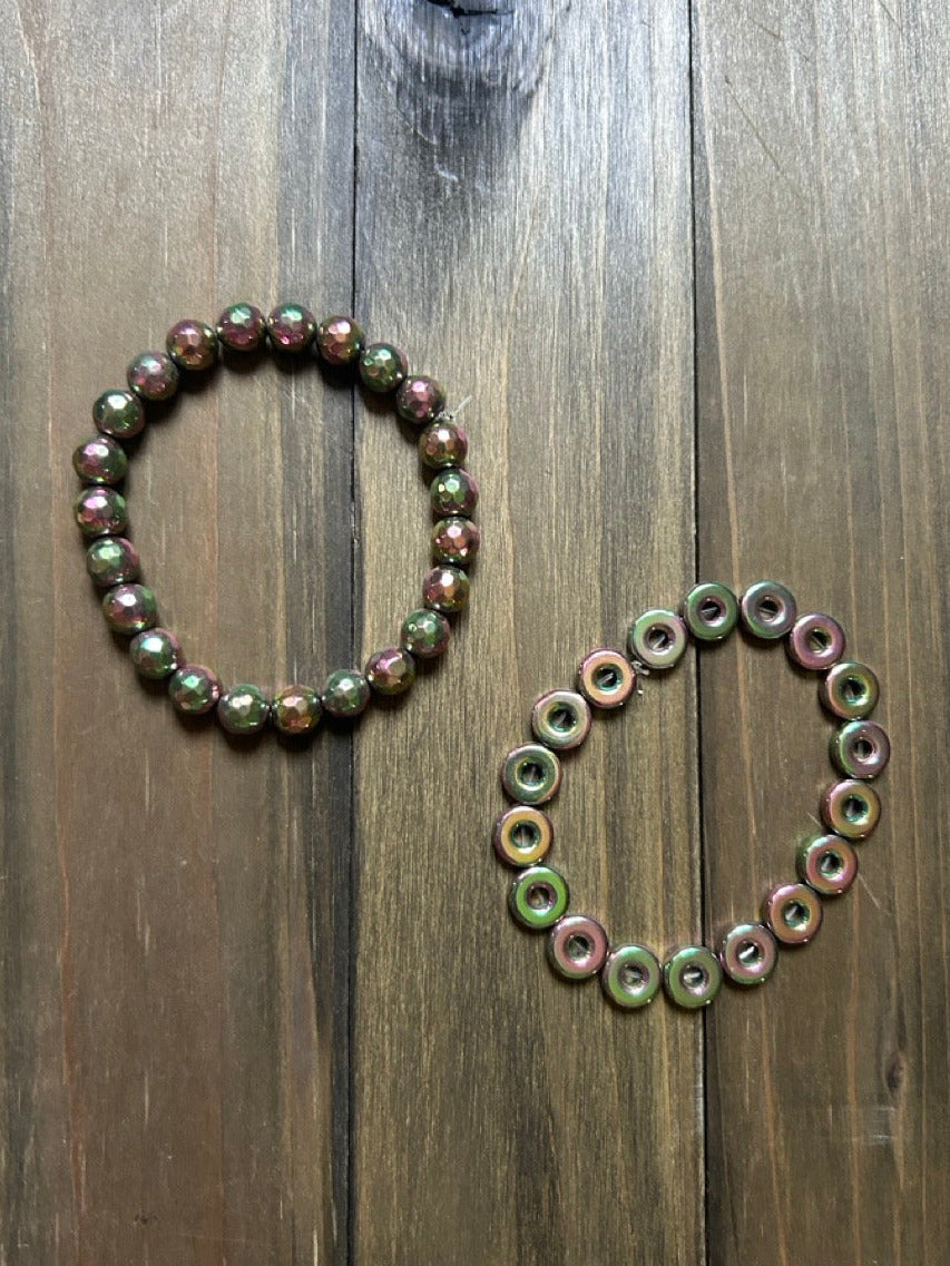 Two beaded bracelets made of multichromatic green and pink stone beads, displayed on a dark wood plank background.