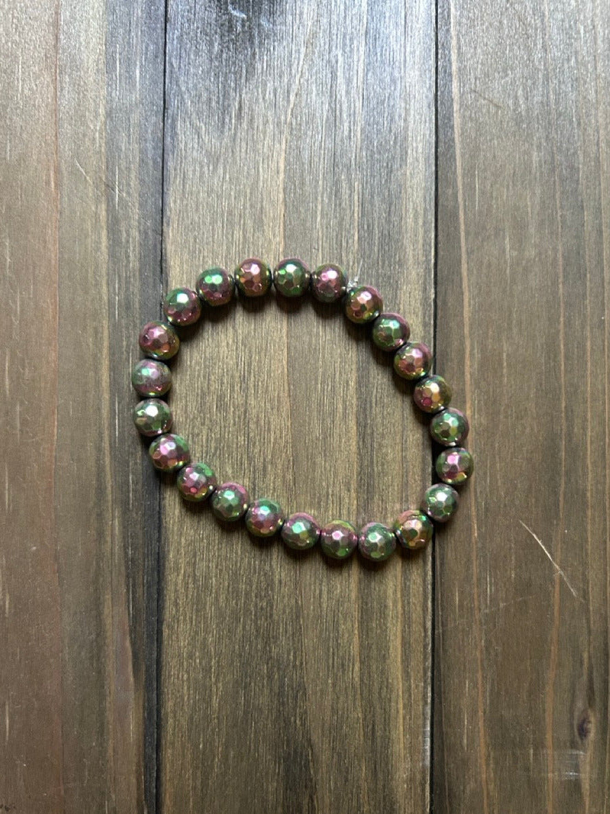 A beaded stretch bracelet made of faceted round beads with a metallic, iridescent finish of green and pink hues. Displayed on a dark wood background.