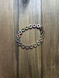 A beaded bracelet made of small iridescent donut-shaped beads in shades of green and pink, on a dark brown wooden surface.