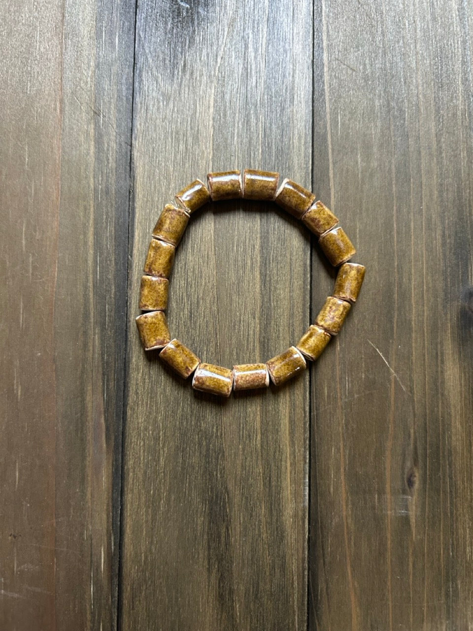 A ceramic beaded stretch bracelet made of cylindrical brown beads, displayed on a dark wood background.