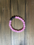 A beaded stretch bracelet made of round, light pink glass beads with a small section of black lava stone beads, displayed on a dark brown wooden surface.