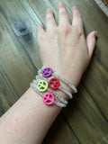 A close-up of a person's wrist wearing four beaded bracelets with colorful peace sign charms, resting on a dark wooden surface.