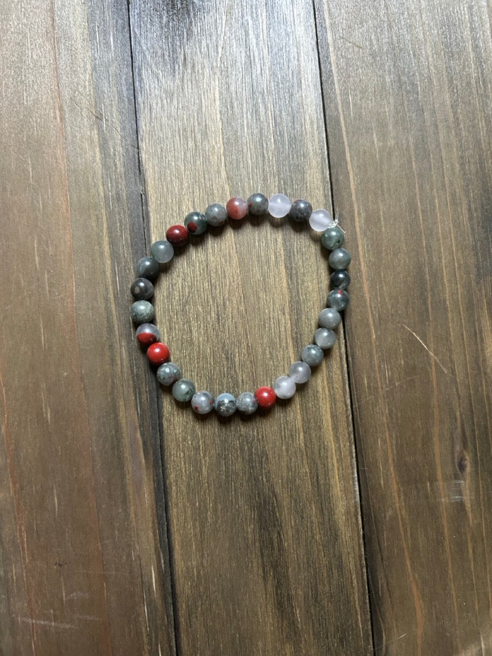 A beaded stretch bracelet made of gray and red marbled beads, displayed on a dark wood background.