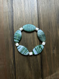 Green and white striped glass beaded bracelet with white spacer beads made of white shell. On a dark wood plank background.