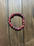 A beaded stretch bracelet made of glossy, round beads with a red, black, and white striped pattern. Displayed on a dark brown wooden surface.