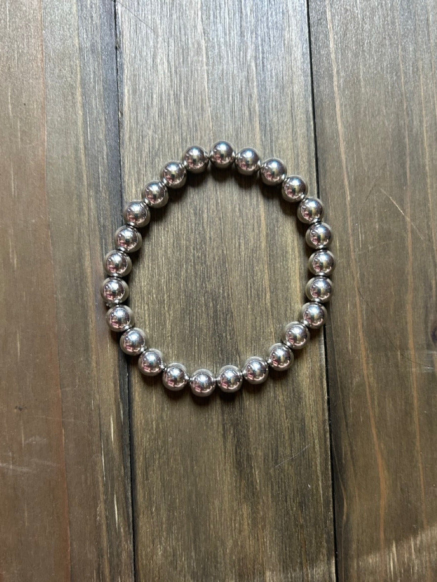 A beaded stretch bracelet made of polished silver glass beads, displayed on a dark brown wooden plank surface.