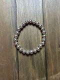 A beaded stretch bracelet made of polished silver glass beads, displayed on a dark brown wooden plank surface.