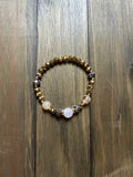 A beaded stretch bracelet featuring faceted gold beads. There are two champagne-colored beads at the front and a clear quartz bead at the center. Displayed on a dark wood background.