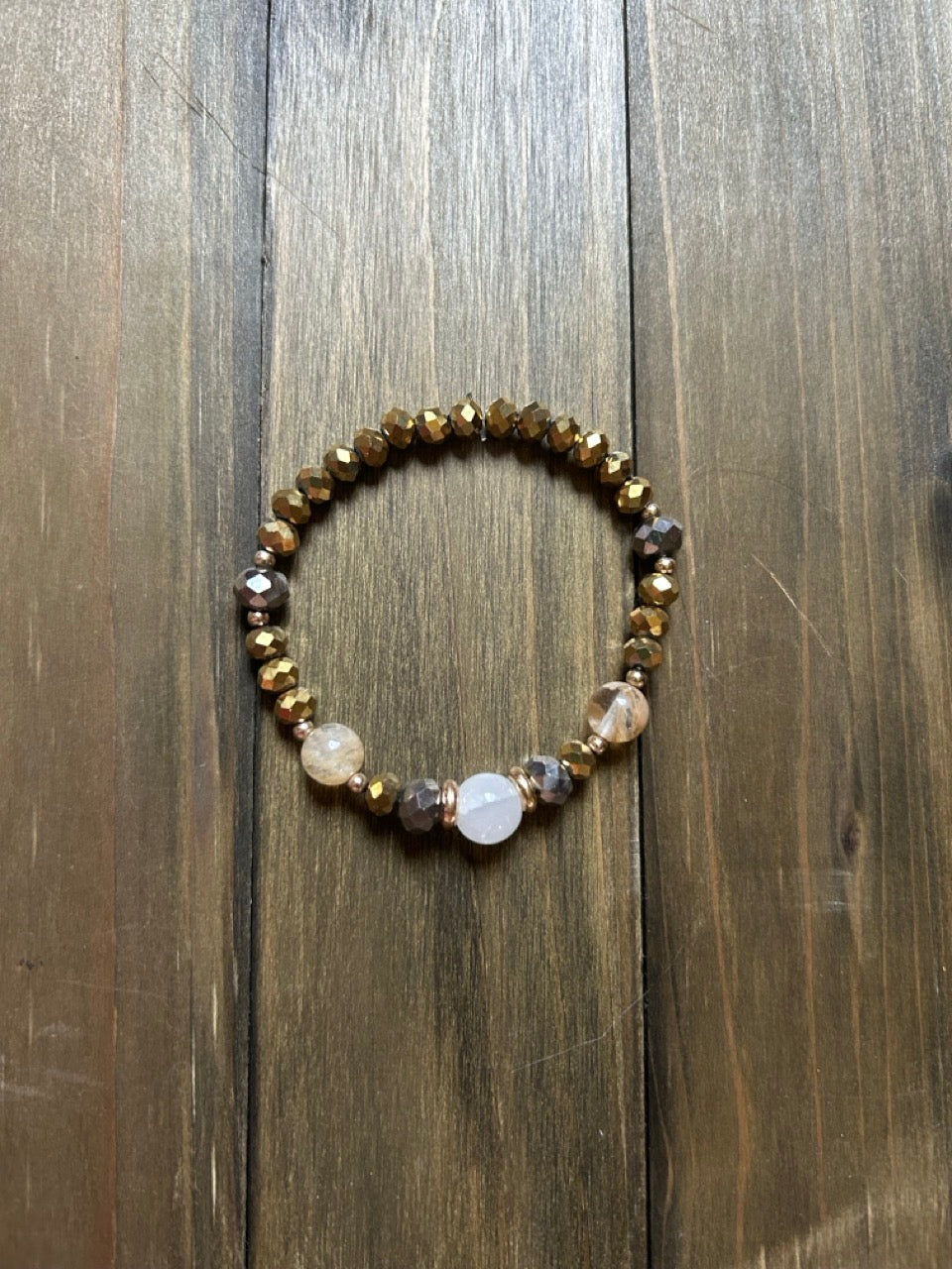 A beaded stretch bracelet featuring faceted gold beads. There are two champagne-colored beads at the front and a clear quartz bead at the center. Displayed on a dark wood background.