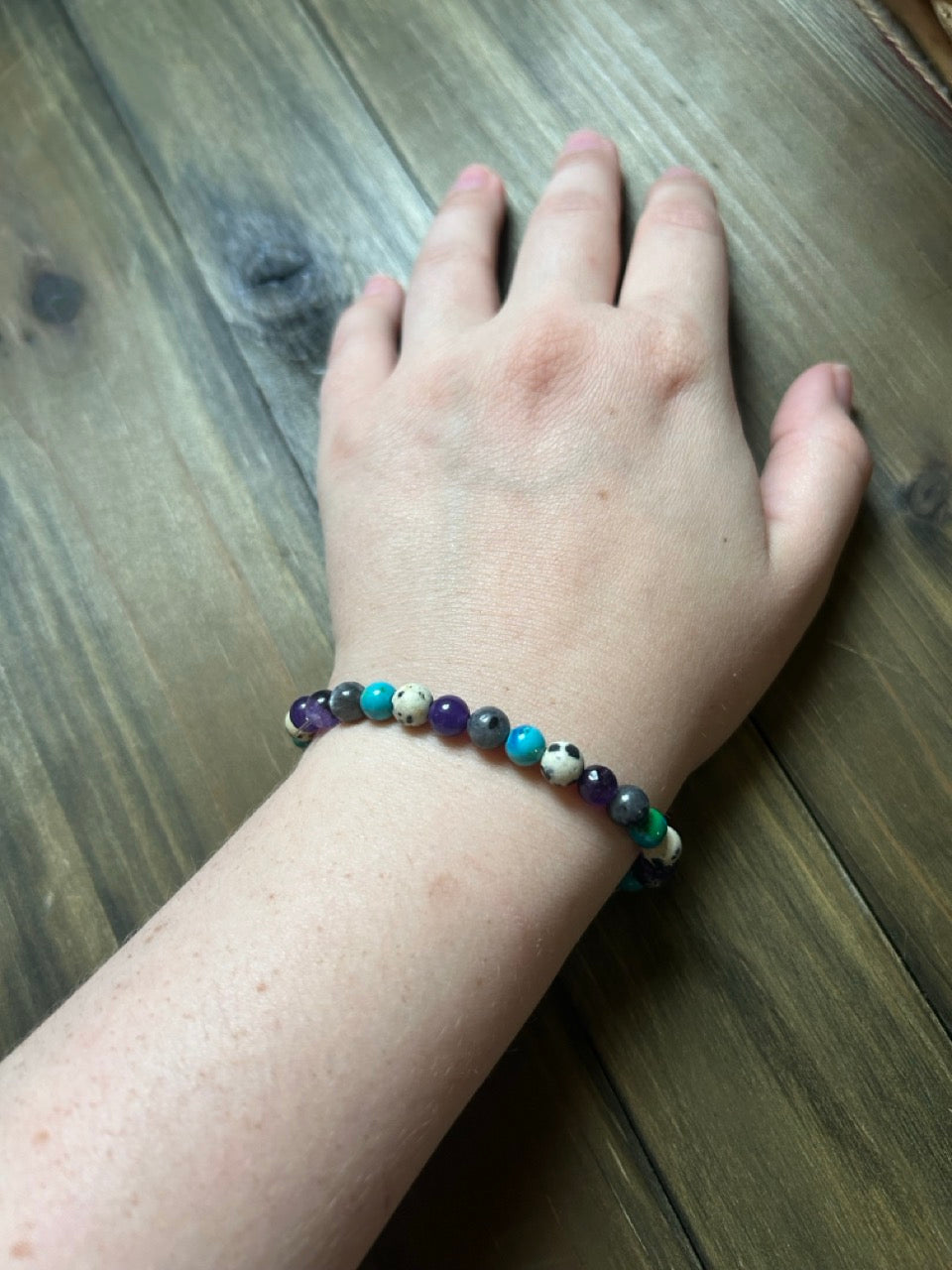 A beaded stretch bracelet with multicolored round beads, worn on a person's wrist resting on a dark wood surface.
